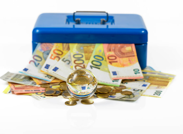 Avro banknotları ve madeni paralar masanın üzerinde duruyor ve cam küreye yansıyan mavi para kutusundan dışarı fırlıyor. - Fotoğraf, Görsel