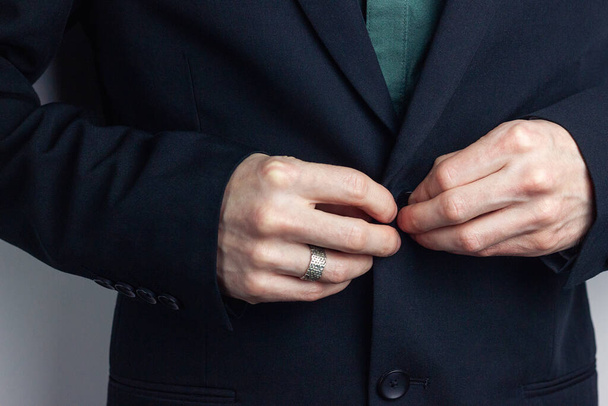 Mannelijke handen van een zakenman in een zakenpak met een ring om zijn vinger een knoop om een jasje. Horizontale oriëntatie foto, zakelijke stijl. - Foto, afbeelding