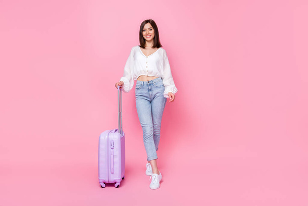Ganzkörperfoto der schönen jungen Frau Koffer Reisebüro Client lächelnd tragen trendige weiße Kleidung isoliert auf rosa Hintergrund. - Foto, Bild