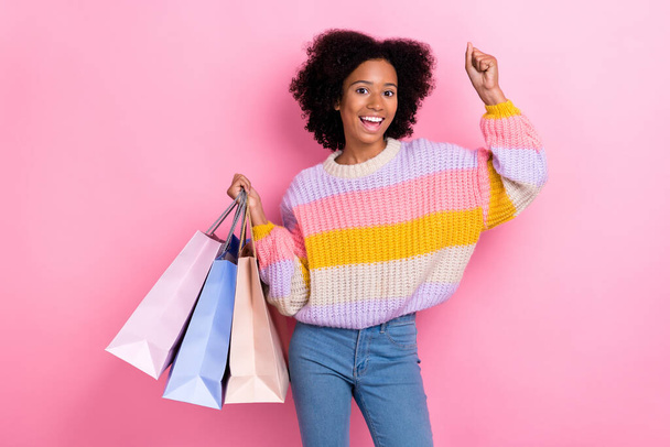 Photo of impressed ecstatic girl with perming coiffure knit sweater hold shopping bags clench fist isolated on pink color background. - Fotografie, Obrázek