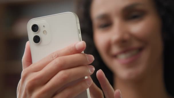 Κοντινό πλάνο θολή ενήλικη Καυκάσια χαμογελαστή γυναίκα κρατώντας κινητό τηλέφωνο δακτυλογράφηση σάρωση περιήγηση στο Internet με smartphone επιλέγοντας στο ηλεκτρονικό κατάστημα χρησιμοποιώντας χρονολόγηση app στο σπίτι γραπτών μηνυμάτων κινητό τηλέφωνο - Πλάνα, βίντεο