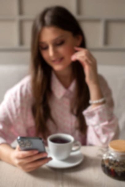 defocused and blurry woman drink tea in cafe searching for information in phone. vertical photo - Foto, Bild