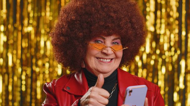 Щаслива радісна старша жінка в шкіряній куртці використовує мобільний телефон, що вводить перегляд, кричить: "Так, дізналися велику перемогу, хороші новини, досягнення лотереї, святкування успіху, перемога
 - Фото, зображення