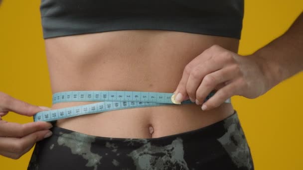 Неузнаваемая девушка измерить размер талии фигуру тела с измерительной лентой проверки желудка сантиметров фитнес-диета спортивные тренировки результат диеты похудения в студии желтый фон - Кадры, видео