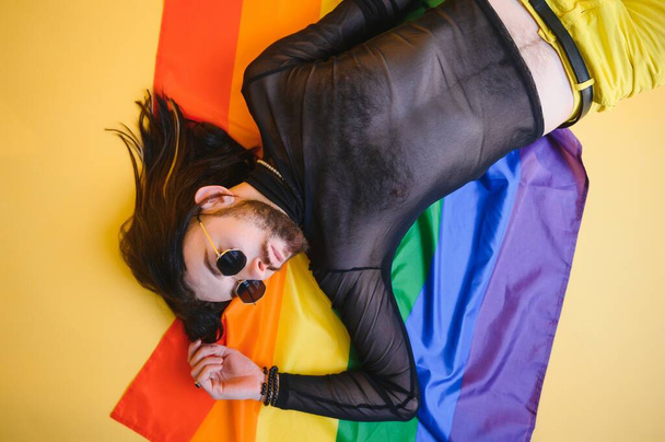 gay man with a gay pride flag smiling and looking away on yellow background. - 写真・画像