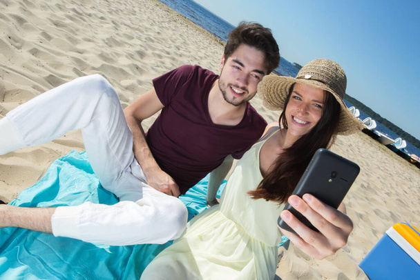 Wspaniała Młoda para siedzi na plaży i robić selfie - Zdjęcie, obraz