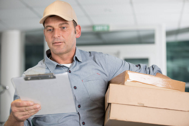 delivery man with box and clipboard on color background - Photo, Image