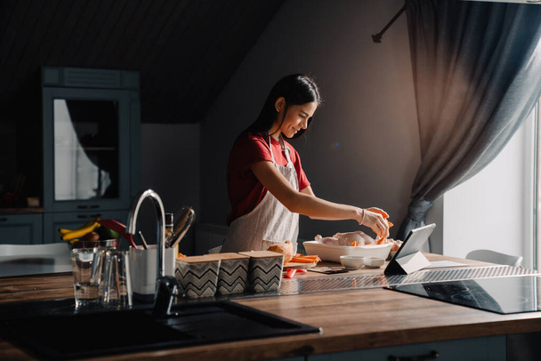 Young hispanic woman using tablet-computer while cooking in kitchen at home - Foto, imagen