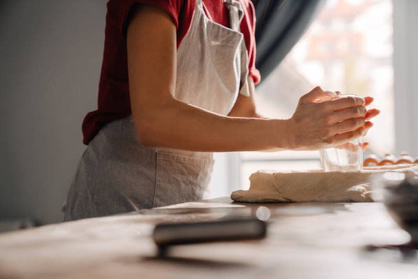 Young hispanic woman wearing apron making pie in kitchen at home - Photo, image
