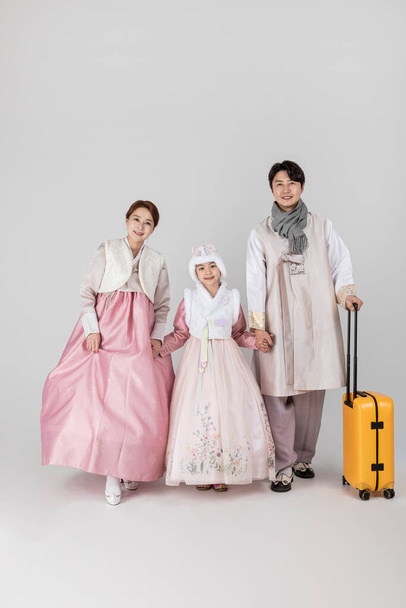 Korean family in Hanbok holding suitcase, against white studio white background - Fotó, kép