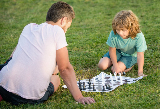 счастливая семья отца человека и сына мальчик играет в шахматы на зеленой траве в парке на открытом воздухе, противник. - Фото, изображение