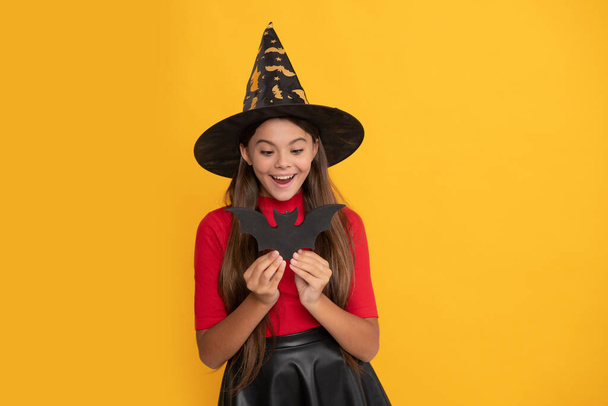 surprised kid with bat wearing witch hat on yellow background, childhood. - Photo, image