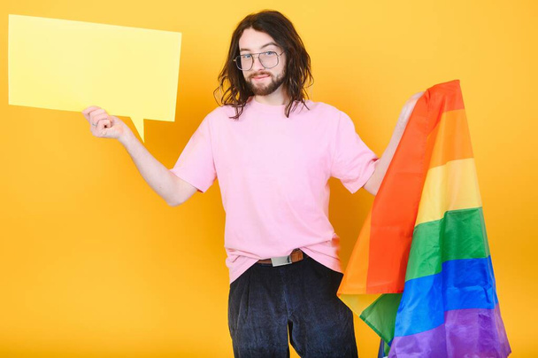 gay man with a gay pride flag smiling and looking away on yellow background - Foto, Bild