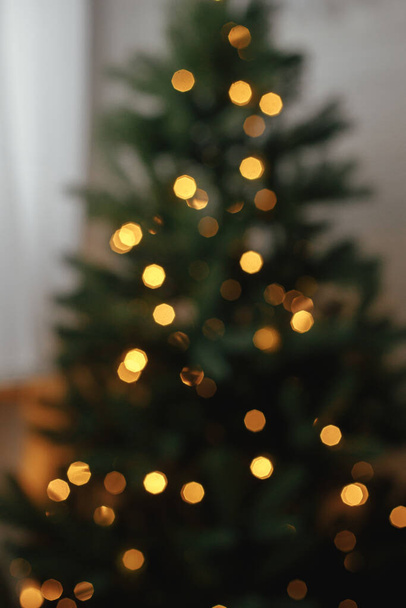 Blurry illuminated christmas tree. Abstract blurred christmas tree with golden lights in evening room. Atmospheric christmas image, magic winter time - Photo, Image