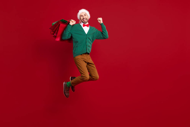 Full body photo of funky jump air excited santa claus lover man raise fists up winter season cheap clothes shopping isolated on red color background. - Foto, imagen