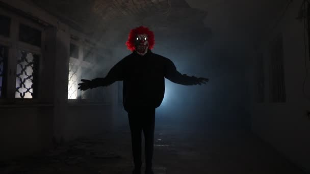 Страшный злой клоун с рыжими волосами, стоящий в разрушенном холле в заброшенном здании ночью. Селективный фокус - Кадры, видео