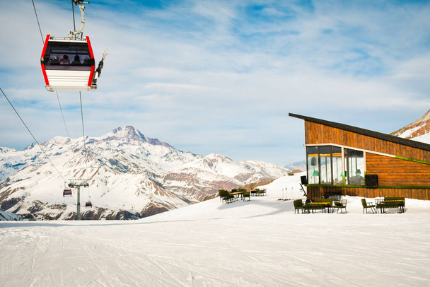 Branco vermelho fechado cabine de elevação de esqui com esquiadores e branco dramático fundo de montanhas nevadas. Estância de esqui reabre. Geórgia férias de inverno em Gudaur. Kobi declives café e área - Foto, Imagem