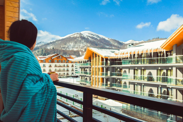 Bakuriani, Georgia - March 5th, 2022: female caucasian tourist in morning drink coffee in balcony in Holiday apartment building on Bakuriani holiday ski resort in Georgia. - Photo, Image