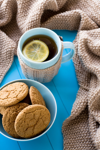 Ένα φλιτζάνι τσάι με λεμόνι, μπισκότα, μπεζ πλεκτή κουβέρτα ψέμα σε  - Φωτογραφία, εικόνα