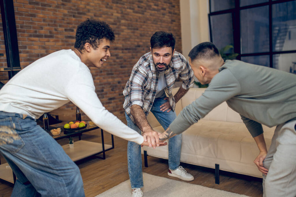 Smiling joyful Arab guy playing rock paper scissors with his pals in the living room - Zdjęcie, obraz