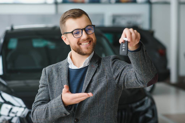 Good looking, cheerful and friendly salesman poses in a car salon or showroom - Fotoğraf, Görsel