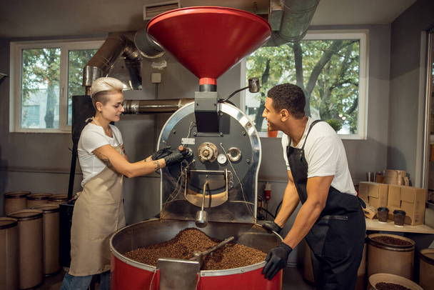 Smiling young roaster and her pleased male colleague checking the roast degree of coffee beans - Foto, Imagen