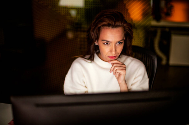 Shot of serious thoughtful business woman sitting at table with computer in office in late evening. - Φωτογραφία, εικόνα