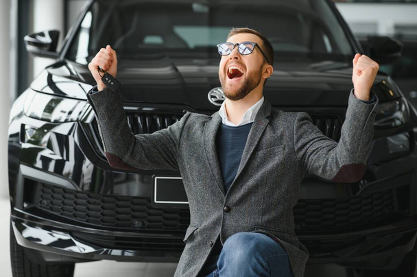 Happy owner of a new car. Emotional handsome man in casual clothes is happy, buying a car in the dealership - Foto, Imagem