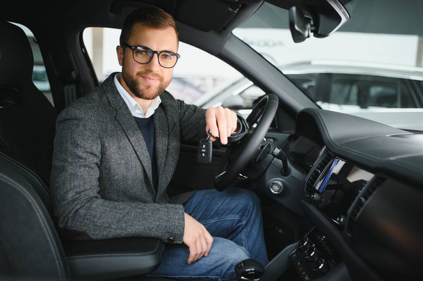 Visiting car dealership. Handsome bearded man is stroking his new car and smiling. - Foto, imagen
