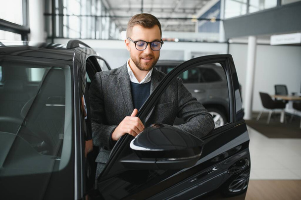 Man adult customer male buyer client wears classic suit white shirt chooses auto wants to buy new automobile touch check car in showroom vehicle salon dealership store motor show indoor. Sales concept - Фото, зображення