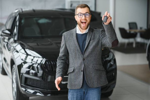 Glücklicher Besitzer eines neuen Autos. Emotional gut aussehender Mann in lässiger Kleidung ist glücklich, kauft ein Auto im Autohaus - Foto, Bild