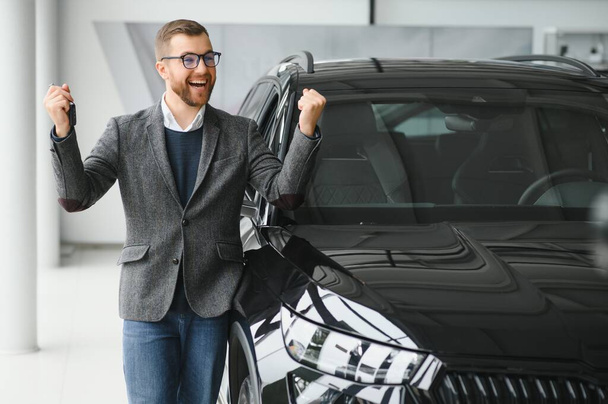 Happy owner of a new car. Emotional handsome man in casual clothes is happy, buying a car in the dealership - Foto, Imagen