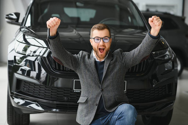 Egy új autó boldog tulajdonosa. Érzelmes jóképű férfi alkalmi ruhákban boldog, vesz egy autót a kereskedésben. - Fotó, kép