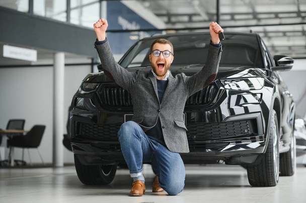 Happy owner of a new car. Emotional handsome man in casual clothes is happy, buying a car in the dealership - Фото, зображення