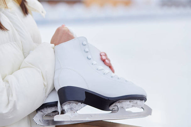 Mujer sosteniendo patines de hielo fuera en el invierno cerca de pista de patinaje. Estilo de vida activo, concepto de sueño. - Foto, imagen