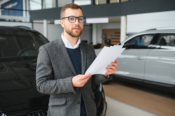 Good looking, cheerful and friendly salesman poses in a car salon or showroom - Photo, image