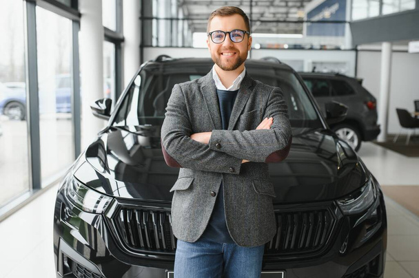 Good looking, cheerful and friendly salesman poses in a car salon or showroom - Фото, изображение