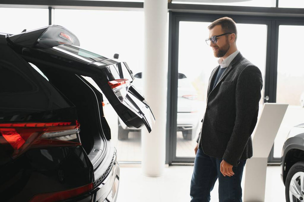 Man adult customer male buyer client wears classic suit white shirt chooses auto wants to buy new automobile touch check car in showroom vehicle salon dealership store motor show indoor. Sales concept - Photo, Image