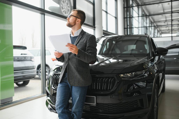 Good looking, cheerful and friendly salesman poses in a car salon or showroom - Foto, Bild