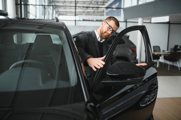 Man minded klant mannelijke koper klant in pak kiezen auto te gaan kijken opzij willen kopen nieuwe auto in de auto showroom - Foto, afbeelding