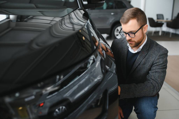 Visiting car dealership. Handsome bearded man is stroking his new car and smiling. - Fotografie, Obrázek