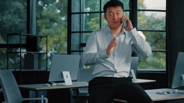 Aasian liikemies yrityksen omistaja pomo perustaja johtaja yritys 40s keski-ikäinen mies soittaa matkapuhelimella 5g yhteys puhuu matkapuhelin kaukainen keskustelu kollegansa kanssa työtä verkossa modernissa toimistossa - Materiaali, video