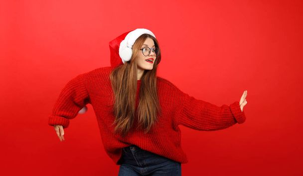 Dancing girl in a santa hat and headphones on a red background, holiday party. Christmas music playlist. - 写真・画像