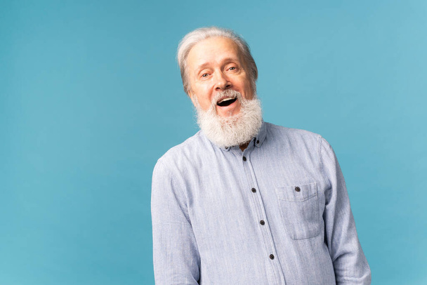 Rentner mit weißem Haar und offenem Bart und strahlendem Lächeln vor blauem Hintergrund - Foto, Bild