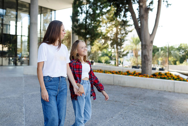 Woman walking and chatting with daughter schoolgirl after school outdoors. Cheerful teen female speaking with mother in good mood. Talk concept. - Photo, Image