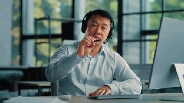 Webcam widok dorosłych pewny Azji mężczyzna biznesmen nauczyciel trener 40 mężczyzna nosi słuchawki siedzieć w nowoczesnym biurze rozmawiać na kamerze odległe połączenie online wideokonferencja biznes webinar gestykulować z piórem - Materiał filmowy, wideo