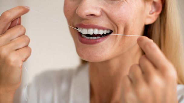 Koncepcja pielęgnacji zębów i leczenia jamy ustnej. Zbliżenie przycięty widok nierozpoznawalnej kobiety w średnim wieku za pomocą nici dentystycznej, robi rano rutynowe, panorama - Zdjęcie, obraz