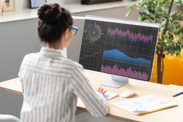 Молодая предпринимательница, анализирующая статистику на экране компьютера, сидящая в офисе, женщина-предприниматель, работающая с финансовыми графиками и диаграммами в Интернете, используя бизнес-программное обеспечение для анализа данных - Фото, изображение