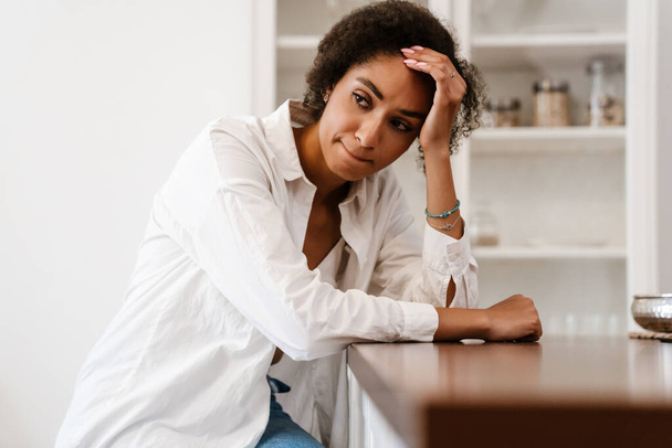 Young black woman being upset and thinking about abortion while sitting on chair at home - Photo, Image