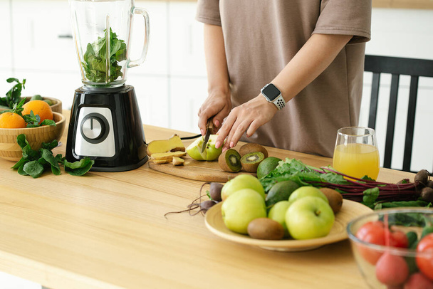 Закрыть женщину, готовящую завтрак из зеленого свежего смузи на кухне, закрыть. Подготовка натурального детоксикационного лимонада за столом на кухне - Фото, изображение